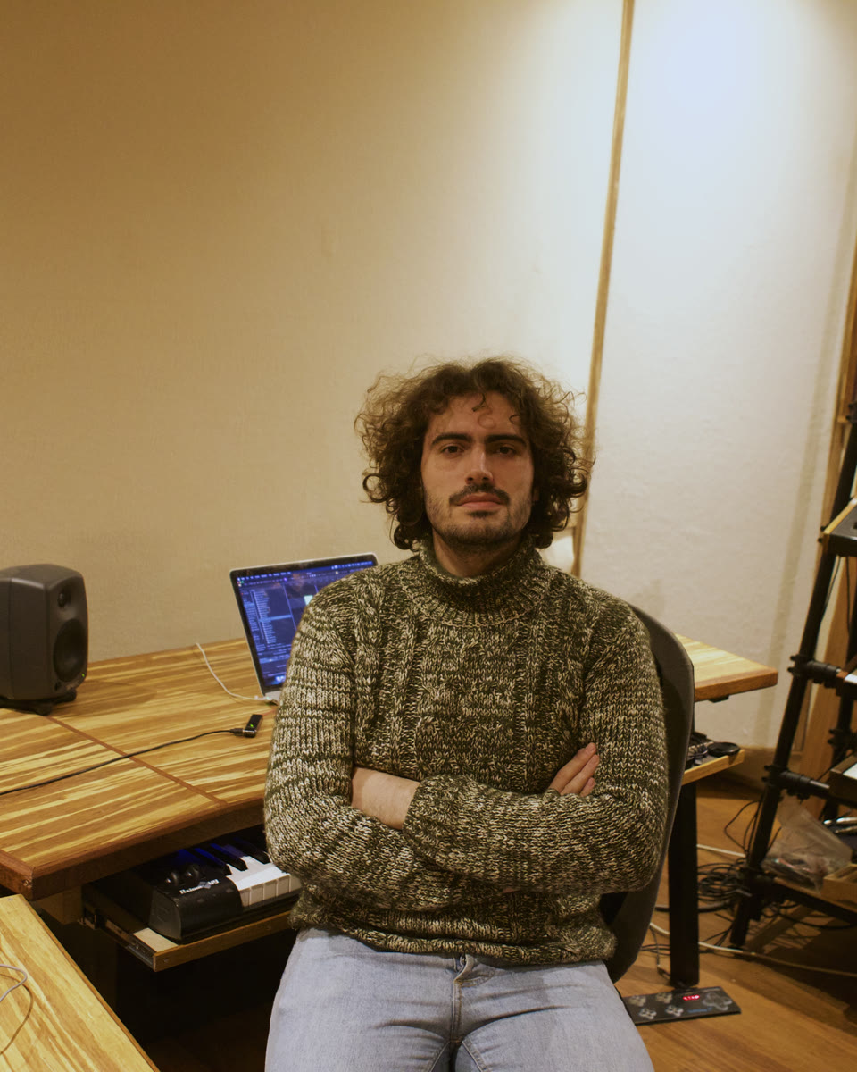 Lorenzo Servali in his studio, arms crossed, in front of a rack of synthesizers